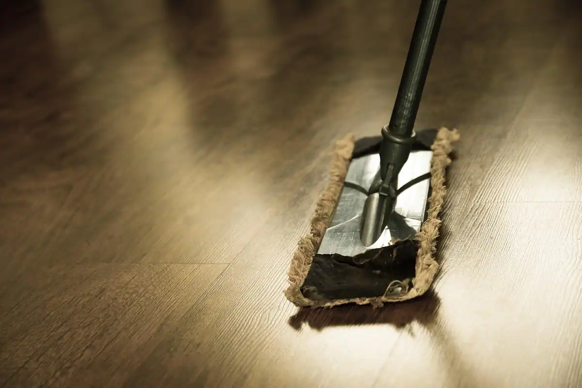 Mop cu mâner lung trecut peste o podea de parchet lucioasă