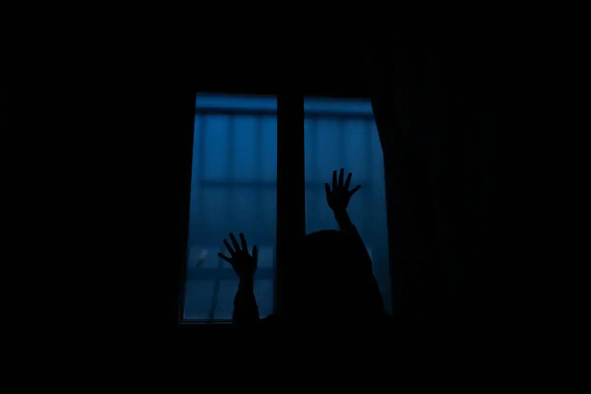 Siluetă de bărbat gânditor în fața unei ferestre, cu o chitară în apropiere
