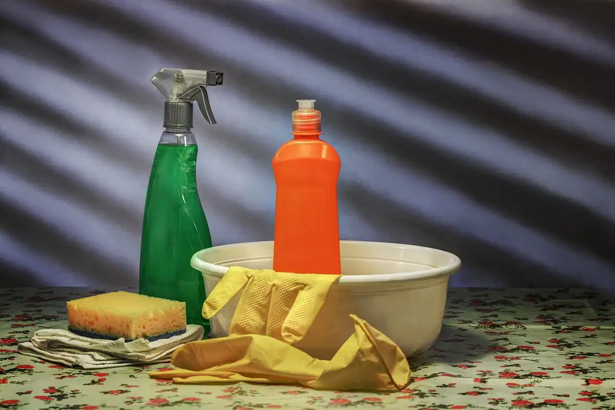 Spray, burete, mănuși de cauciuc și lighean pe o față de masă florală