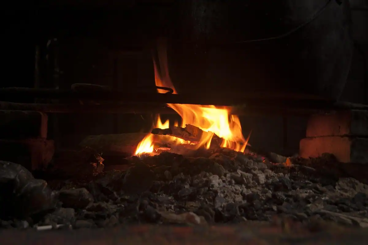 Foc aprins în vatră, cu lemne și cenușă în jur